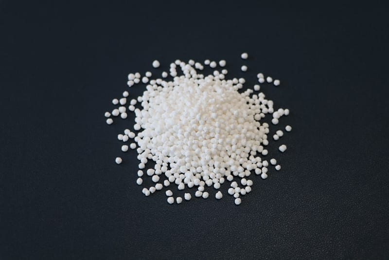 A loose pile of white prilled urea on a dark surface